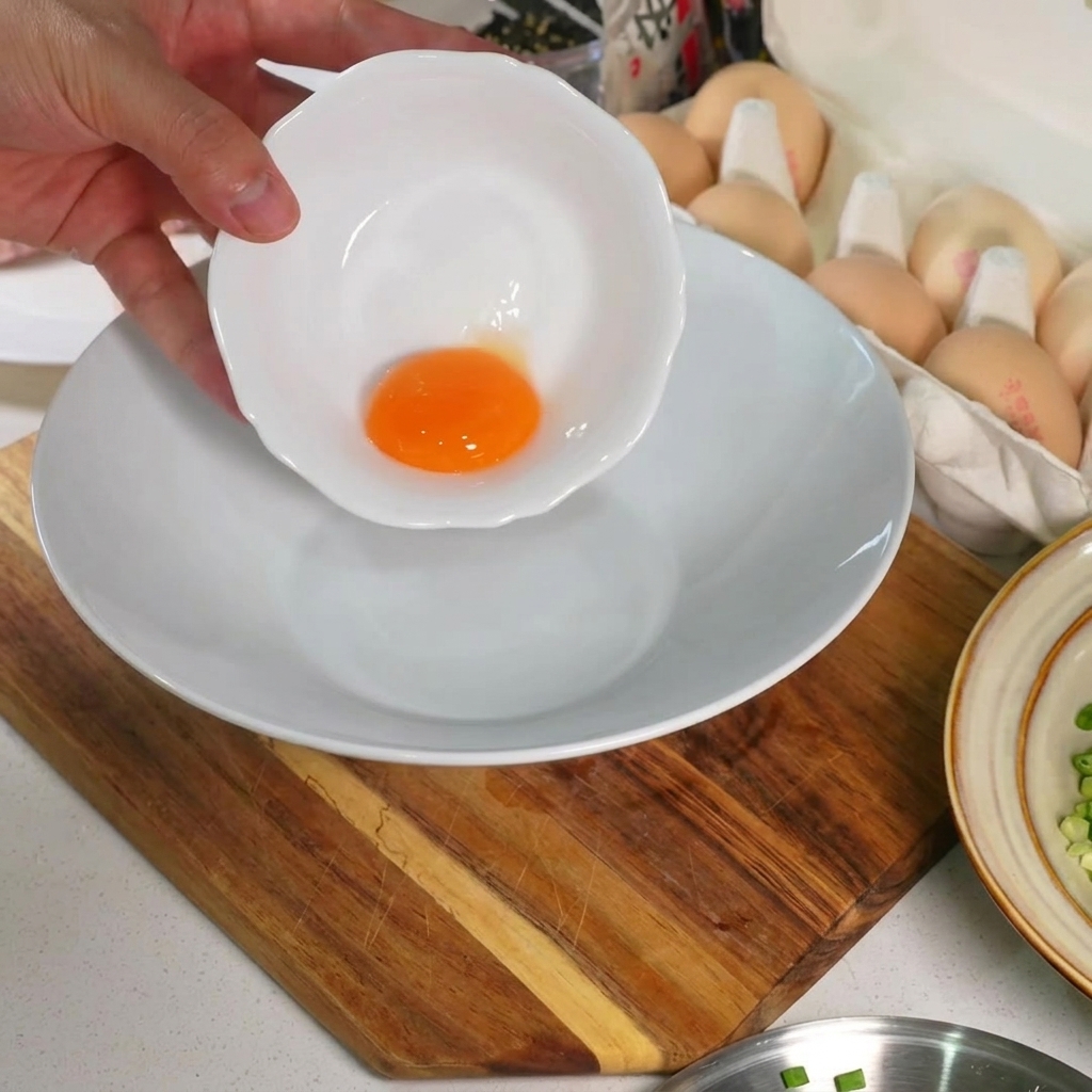 Un singolo, vibrante tuorlo duovo crudo sul fondo di una ciotola di ceramica bianca.
