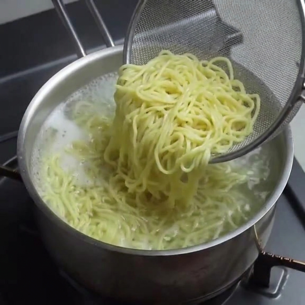 Noodles cotti sollevati da una pentola con un colino a rete.
