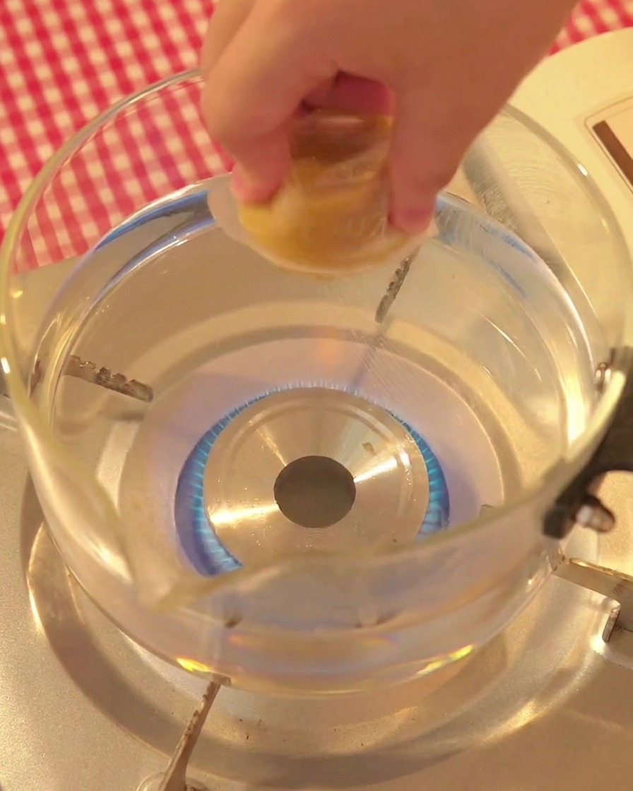 Una mano che mette un dado di brodo di pollo in una pentola dacqua bollente.