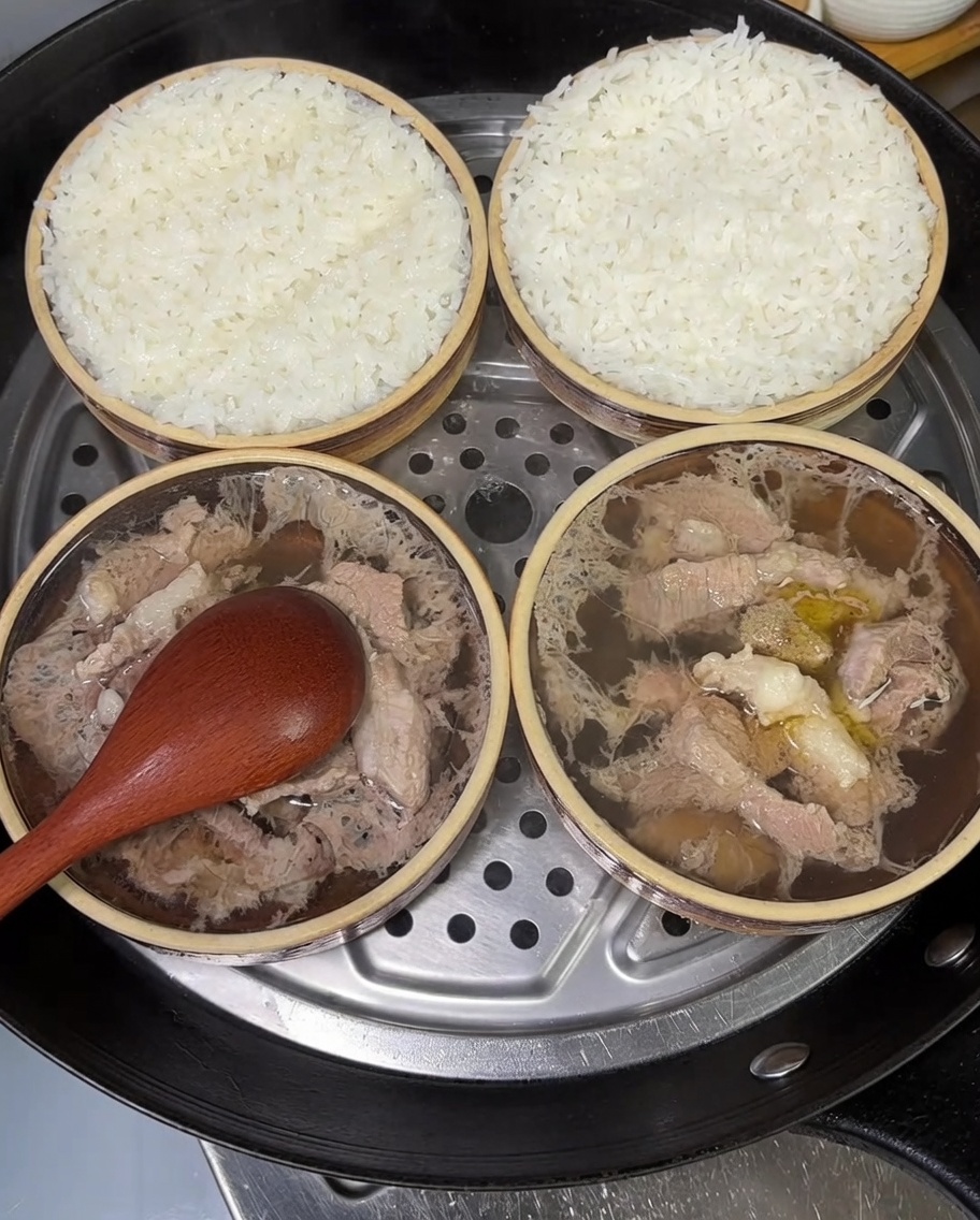 Due piccole ciotole di maiale e riso al vapore guarnite con cipollotti freschi tritati.