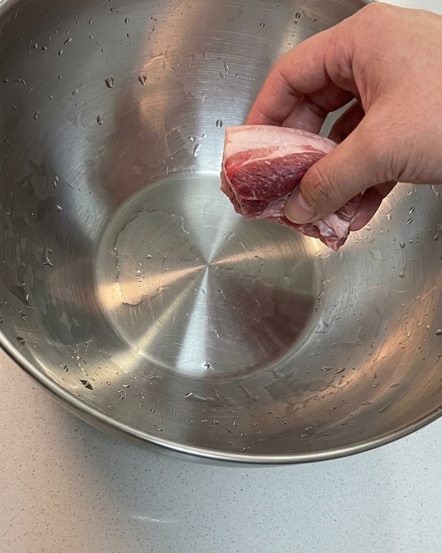 Pancetta e ossa di maiale in ammollo in una grande ciotola dacqua fredda.