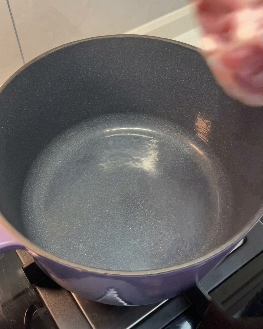 La pancetta e le ossa di maiale sciacquate vengono messe in una grande pentola viola.