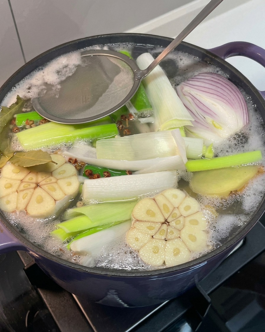 Un colino in metallo rimuove la schiuma grigia dalla superficie del brodo in ebollizione.