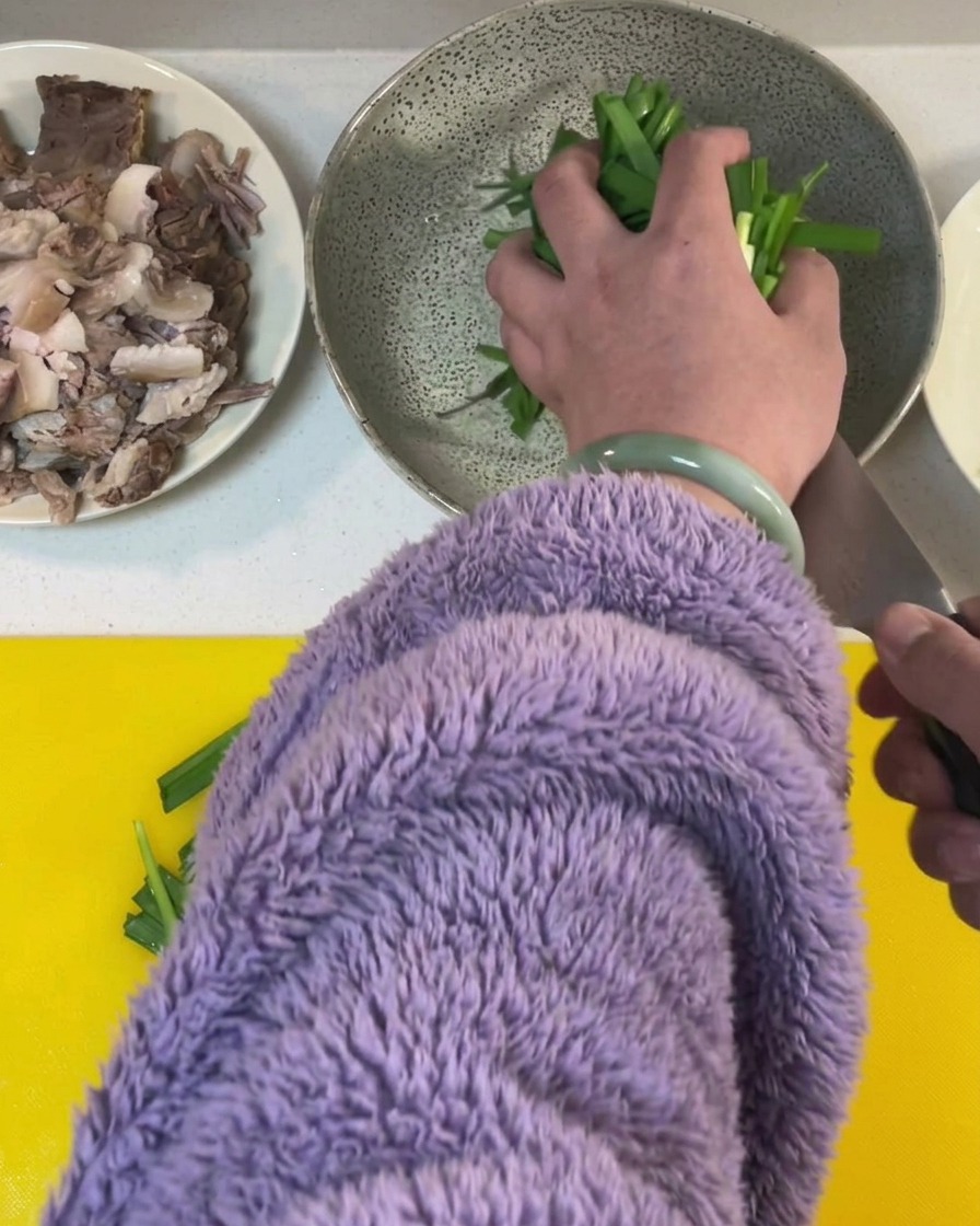 Erba cipollina fresca tagliata a segmenti su un tagliere giallo brillante.