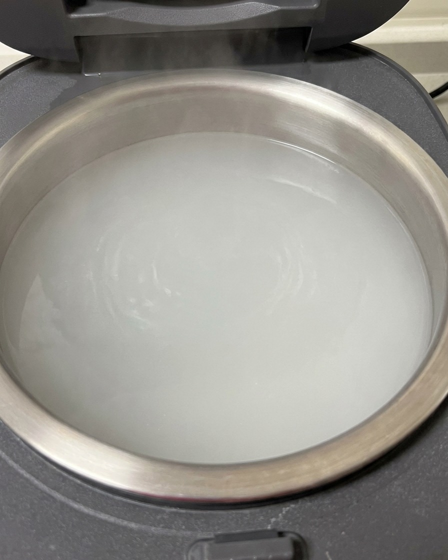 Primo piano di costine di maiale crude immerse in una pentola di cuociriso piena di acqua bollente.