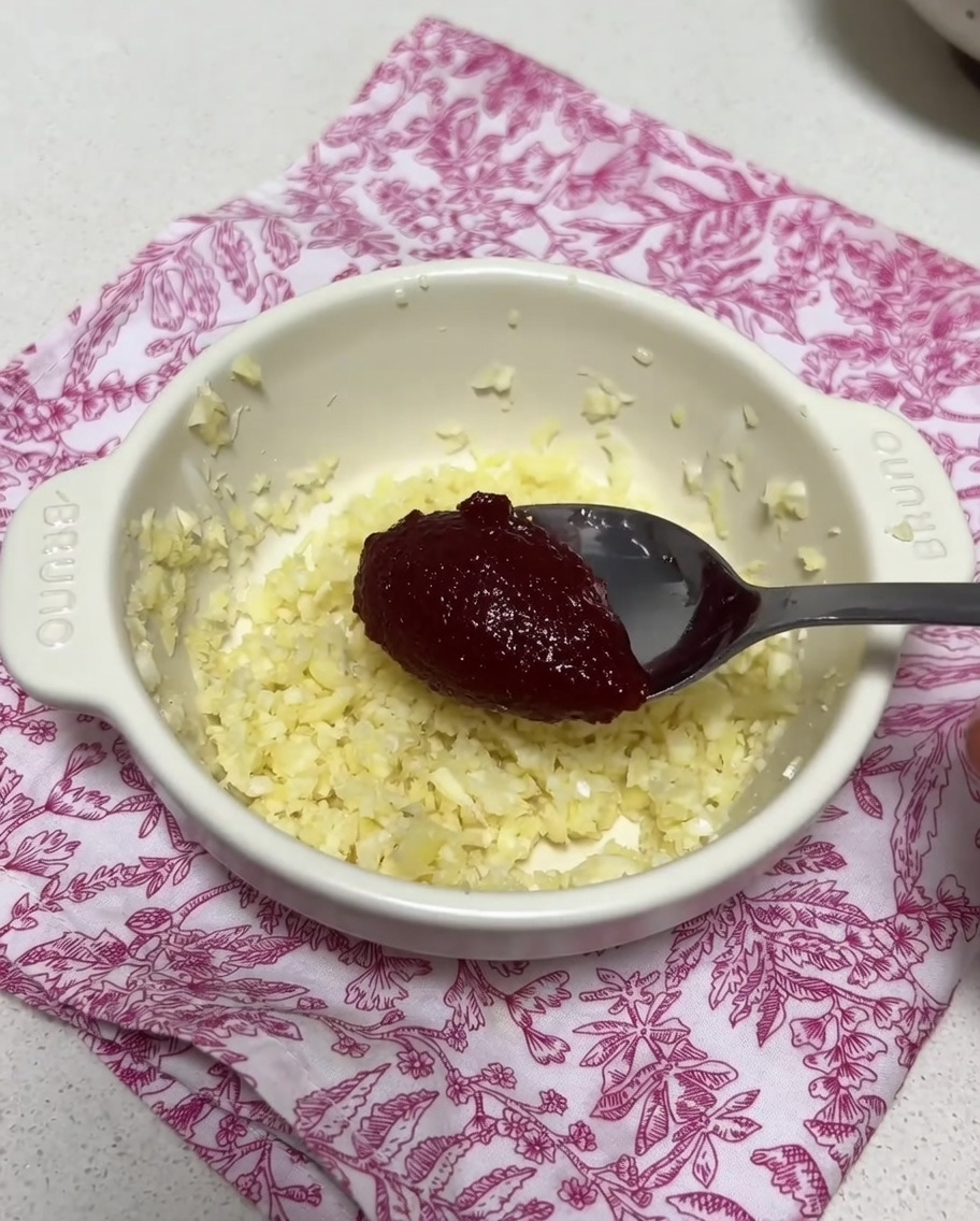 Una ciotolina con aglio tritato e una dose di pasta di peperoncino coreana mischiate con un cucchiaio di brodo.
