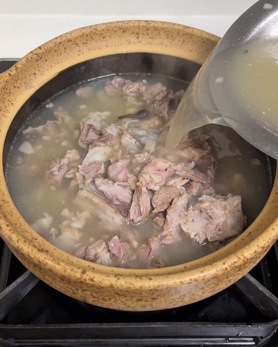 Brodo di carne caldo e opaco versato da un contenitore in acciaio nel tegame con carne e germogli.