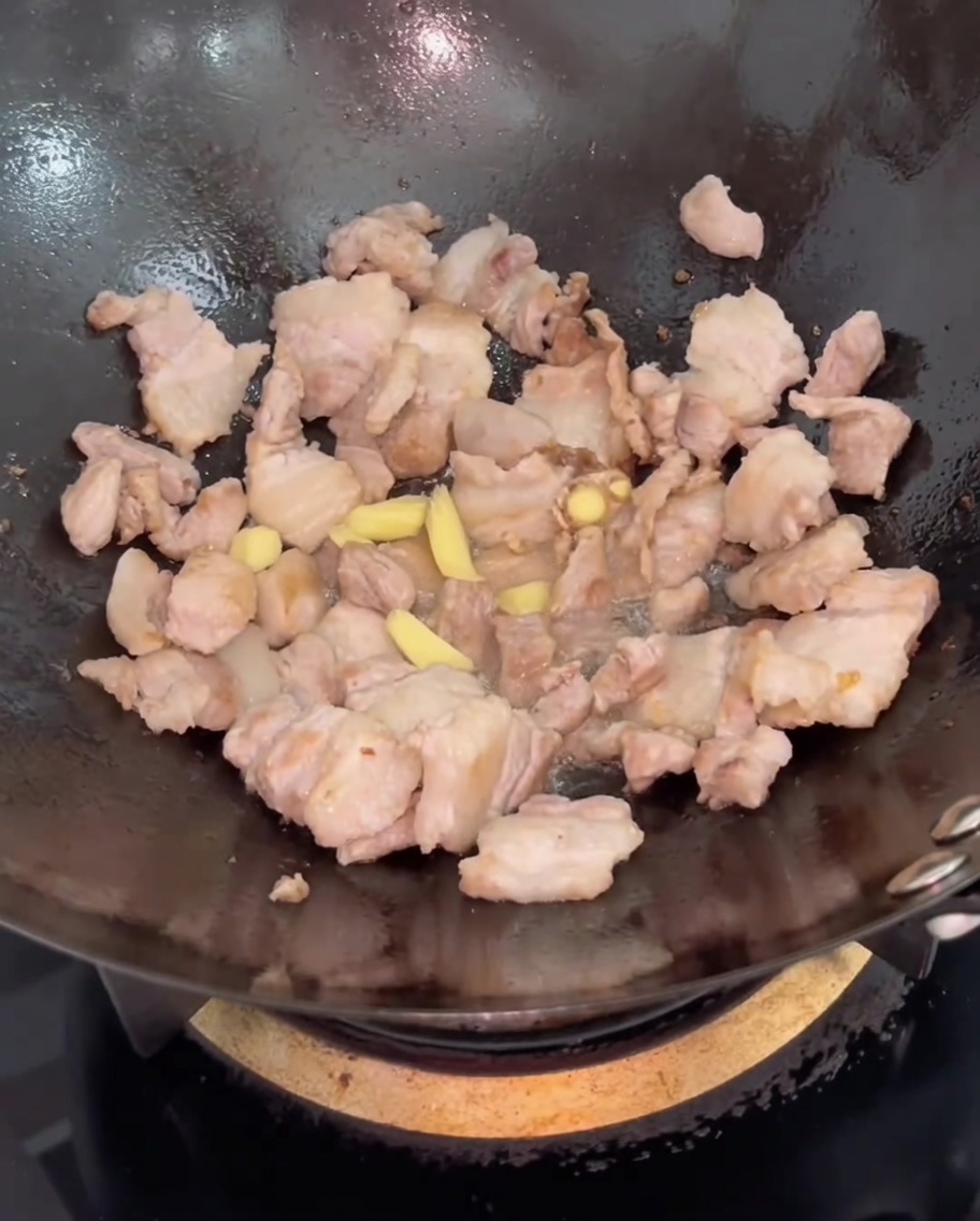 Fette di zenzero fresco aggiunte alla pancetta nel wok.