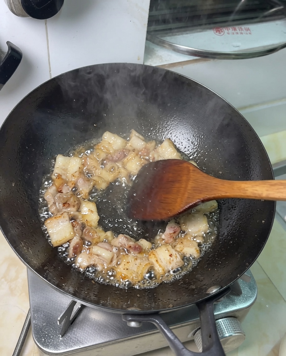 Pezzi di pancetta che friggono nel proprio grasso in un wok.
