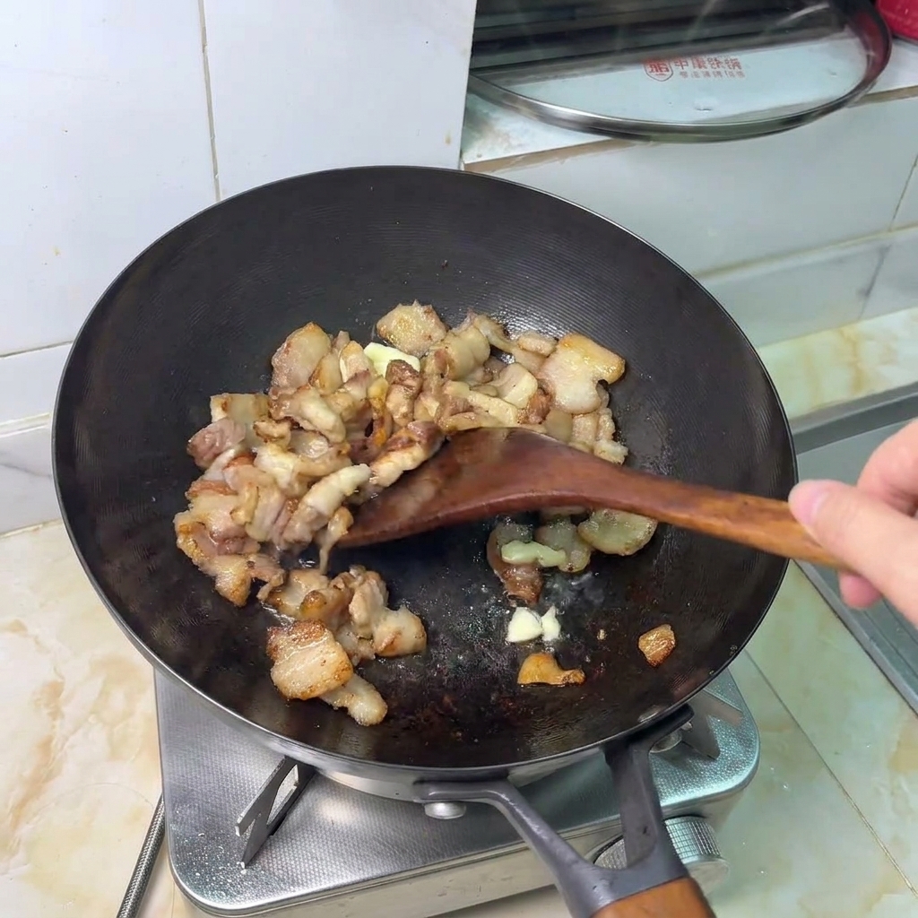 Spicchi daglio schiacciati che soffriggono con i pezzi di pancetta dorati.