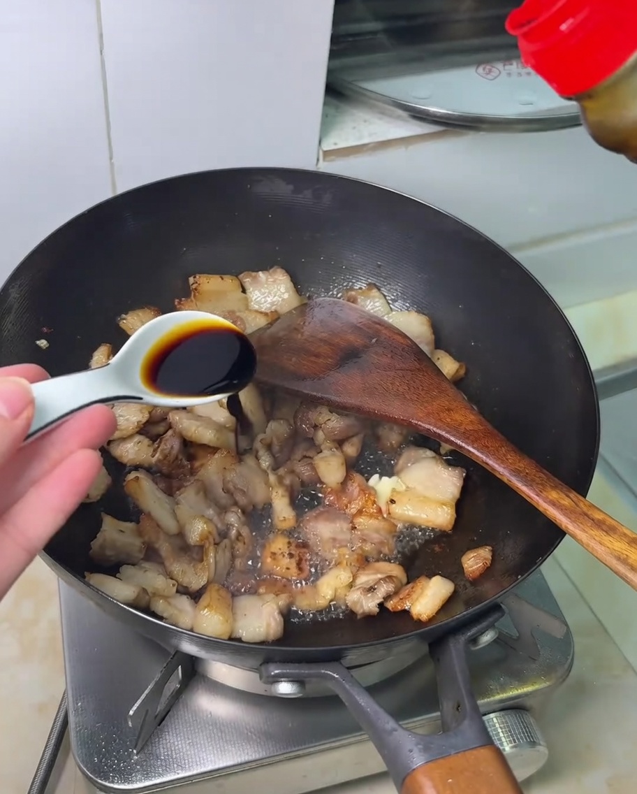 Salsa di soia versata sopra la pancetta saltata in un wok.