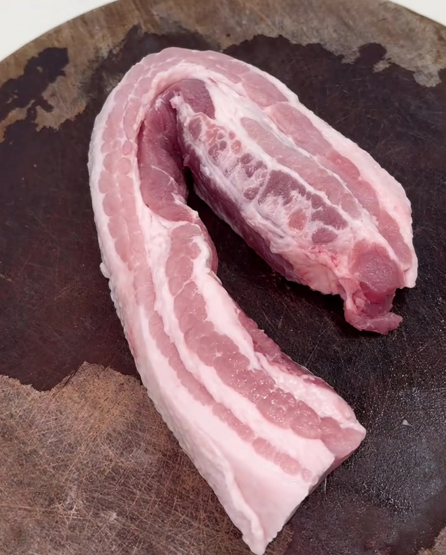 Fettine di pancetta che rosolano in un wok caldo su un fornello.