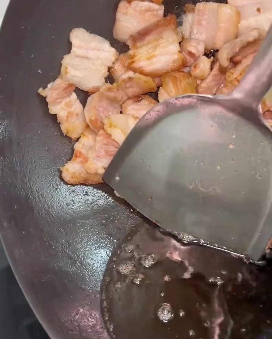 Una spatola di metallo sposta la pancetta di lato mentre il grasso in eccesso viene rimosso dal wok.