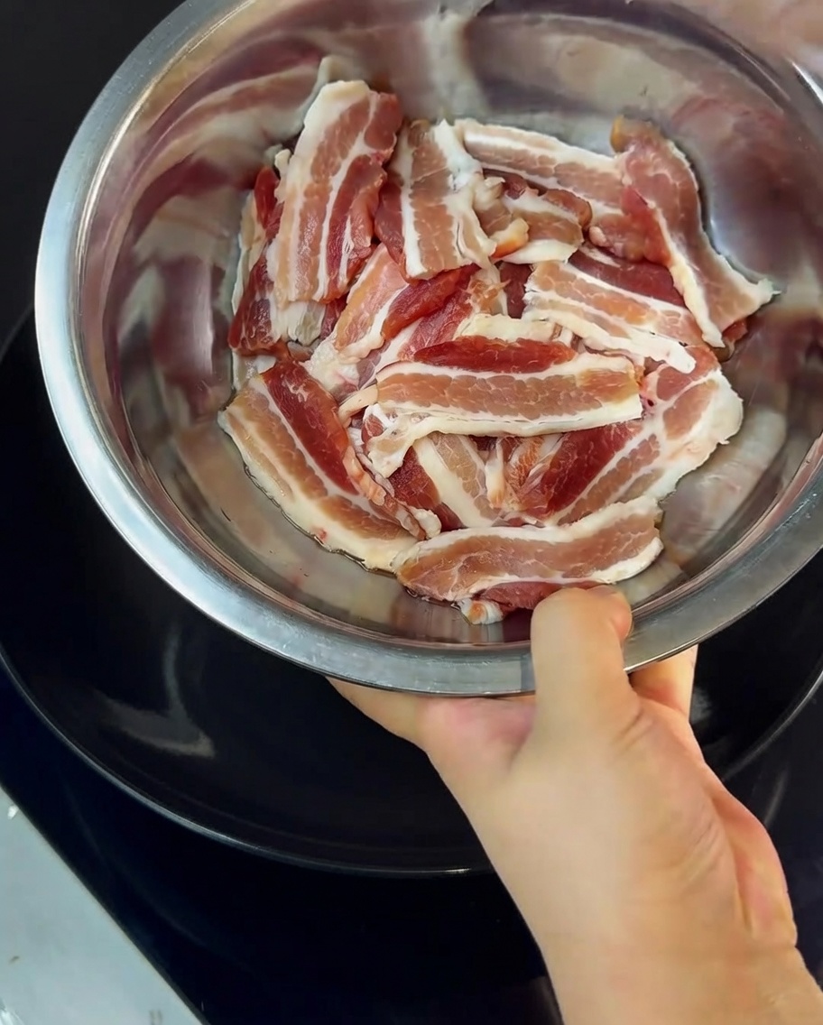 Primo piano di fette di pancetta mescolate con amido di mais in una ciotola di metallo.
