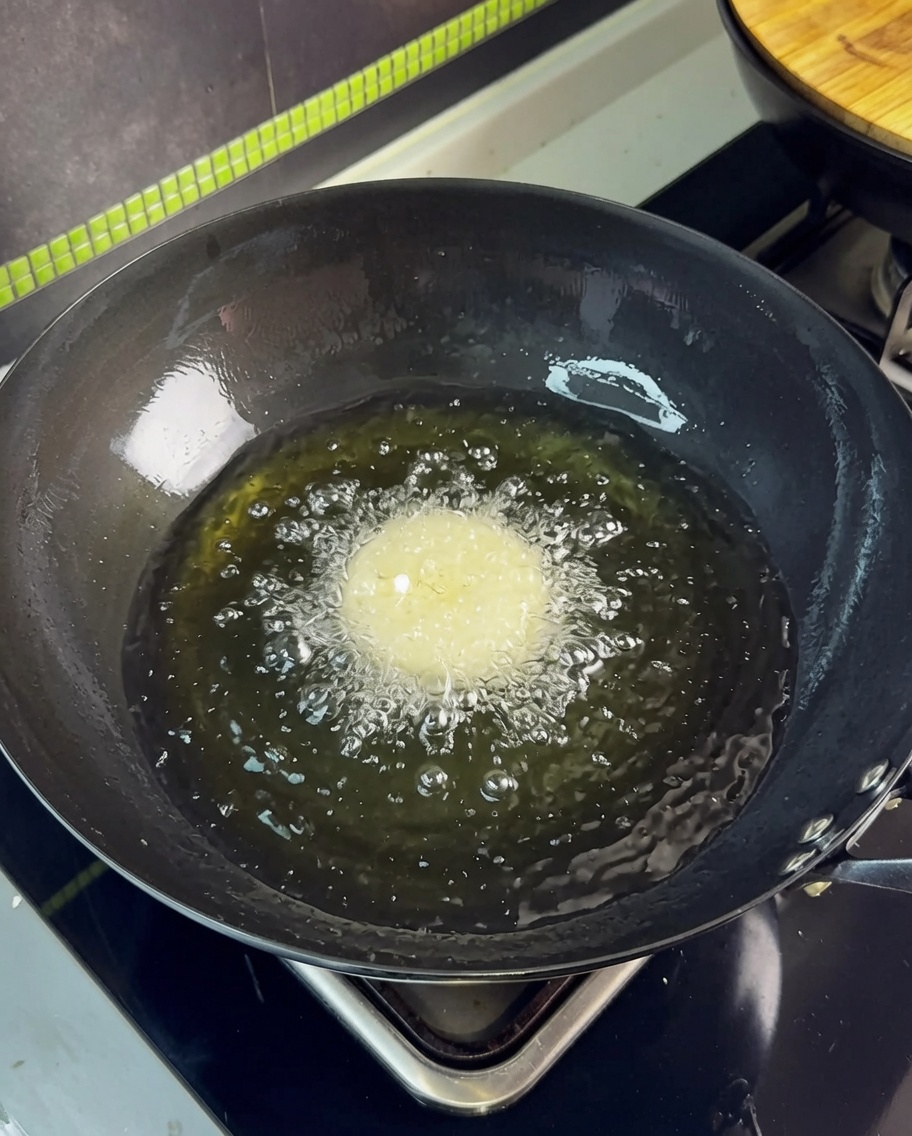 Una singola fetta di pancetta immersa nellolio caldo in un wok, creando bollicine vigorose.