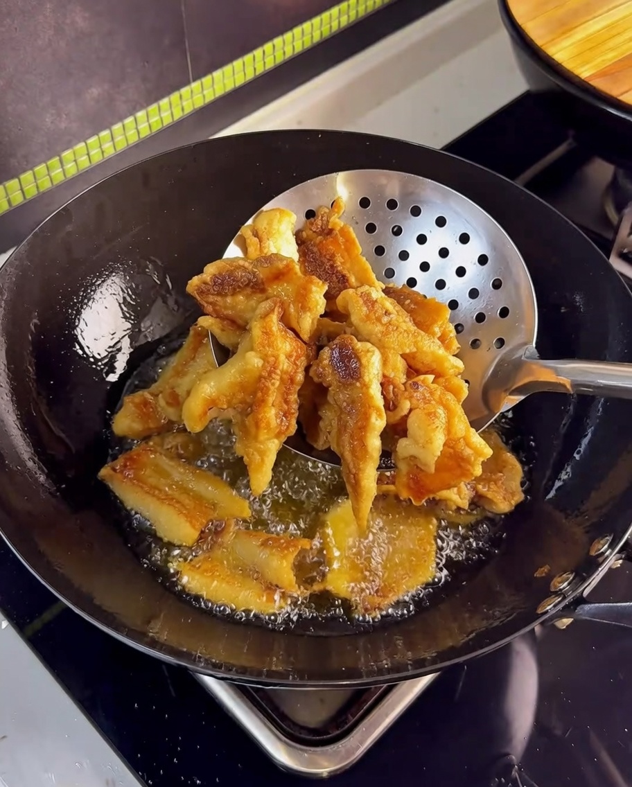 Pancetta croccante dorata estratta dallolio caldo con un ragno da cucina in acciaio inossidabile.