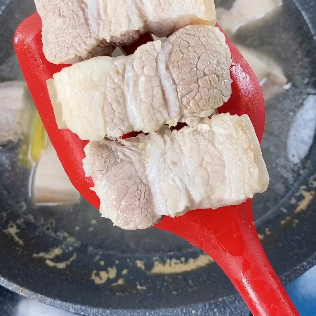 Pezzi di pancetta sbollentata sollevati dallacqua bollente con una spatola rossa.