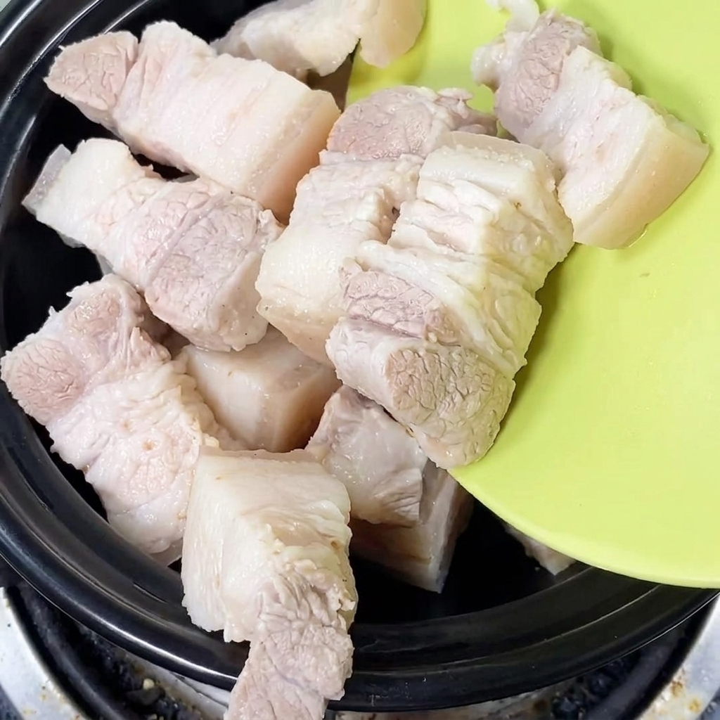 Pezzi di pancetta fresca sbollentata messi in un tegame di terracotta nero.