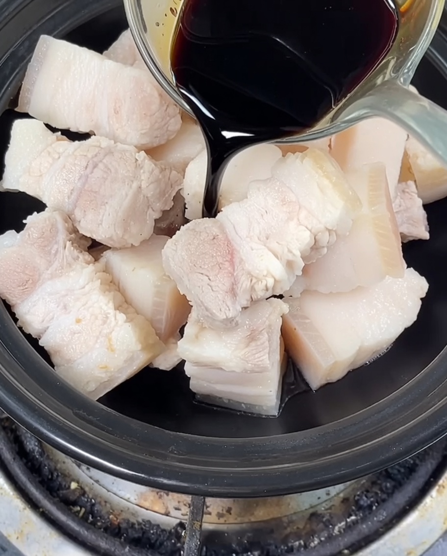 Salsa di soia scura e chiara versata sulla pancetta in un tegame di terracotta, con aggiunta di zucchero cristallizzato.