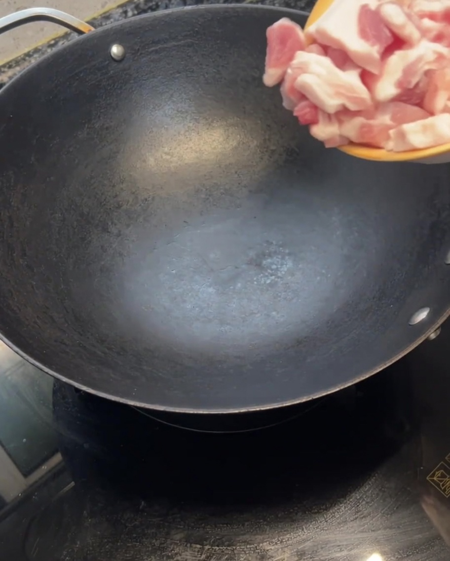 Fette di pancetta cruda inserite in un wok caldo e vuoto.