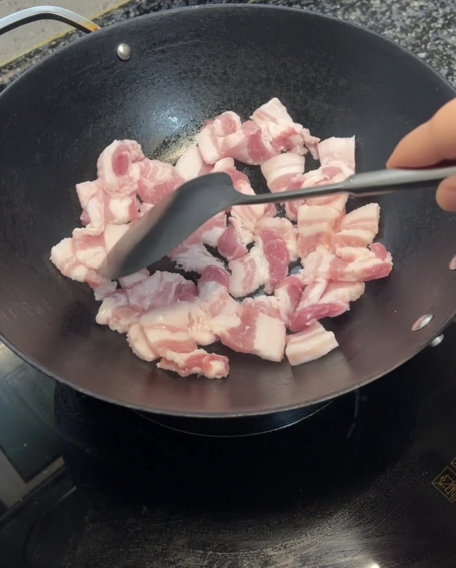 Fette di pancetta saltate nel wok con una spatola, che iniziano a dorarsi.