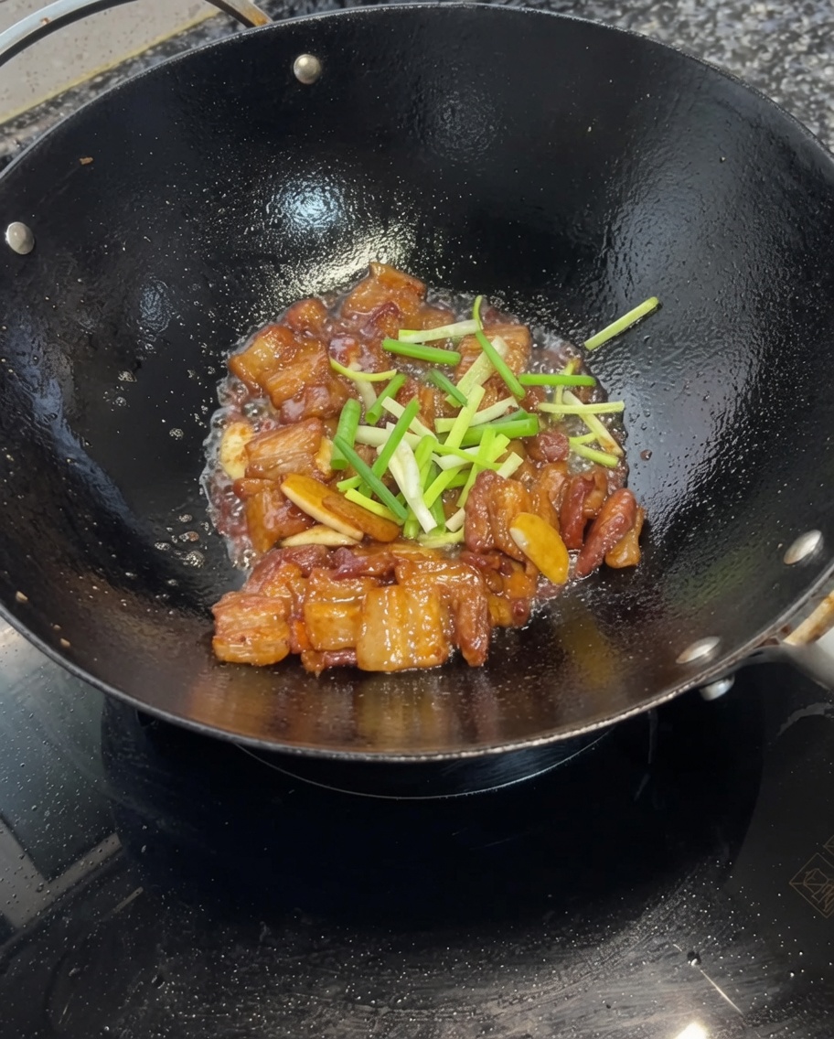 Segmenti di cipollotto tritato mescolati con la pancetta glassata alla soia nel wok.