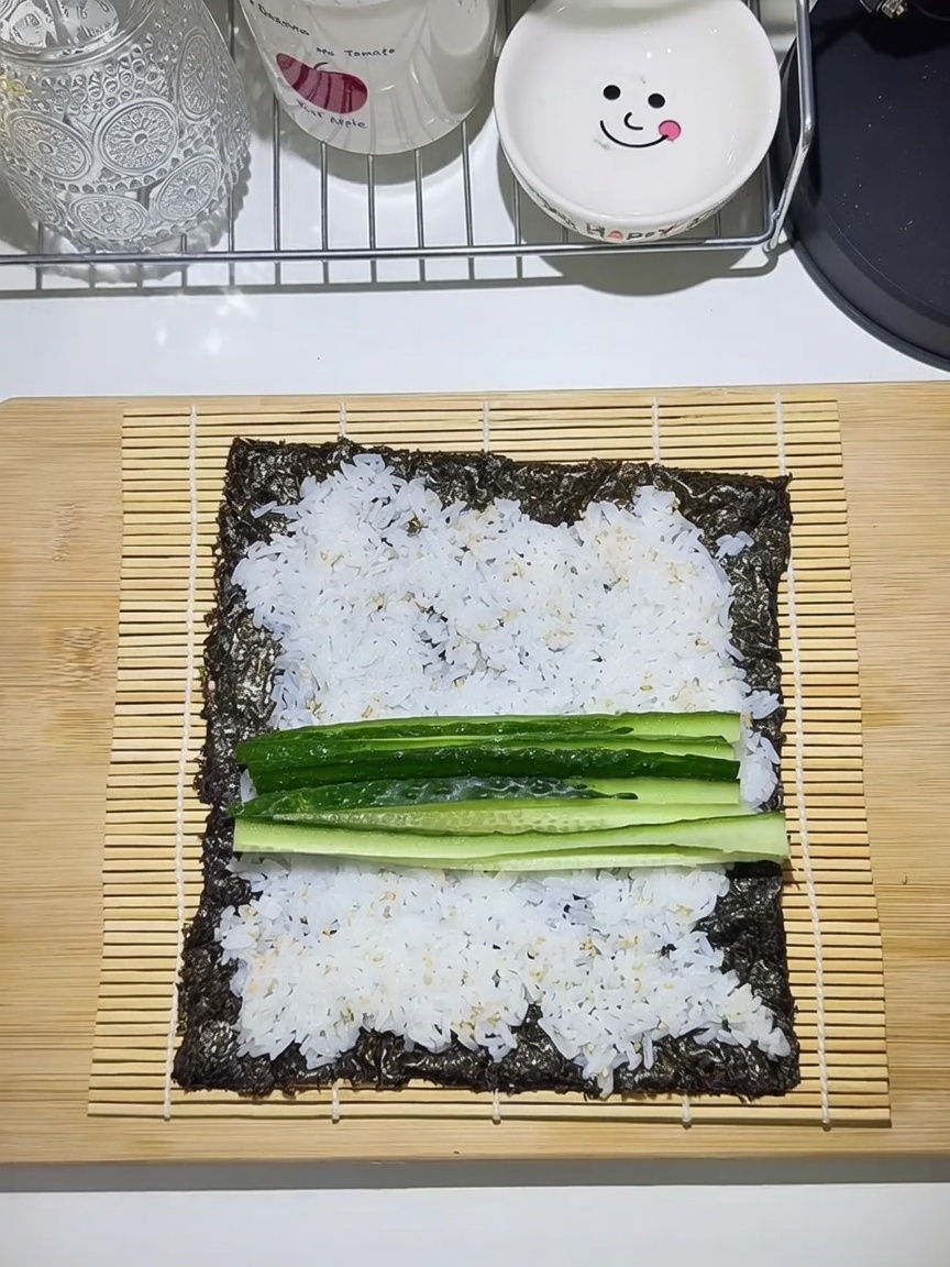 Stuoia di bambù con foglio di alga, riso e strati di cetriolo, carota, uovo e manzo.