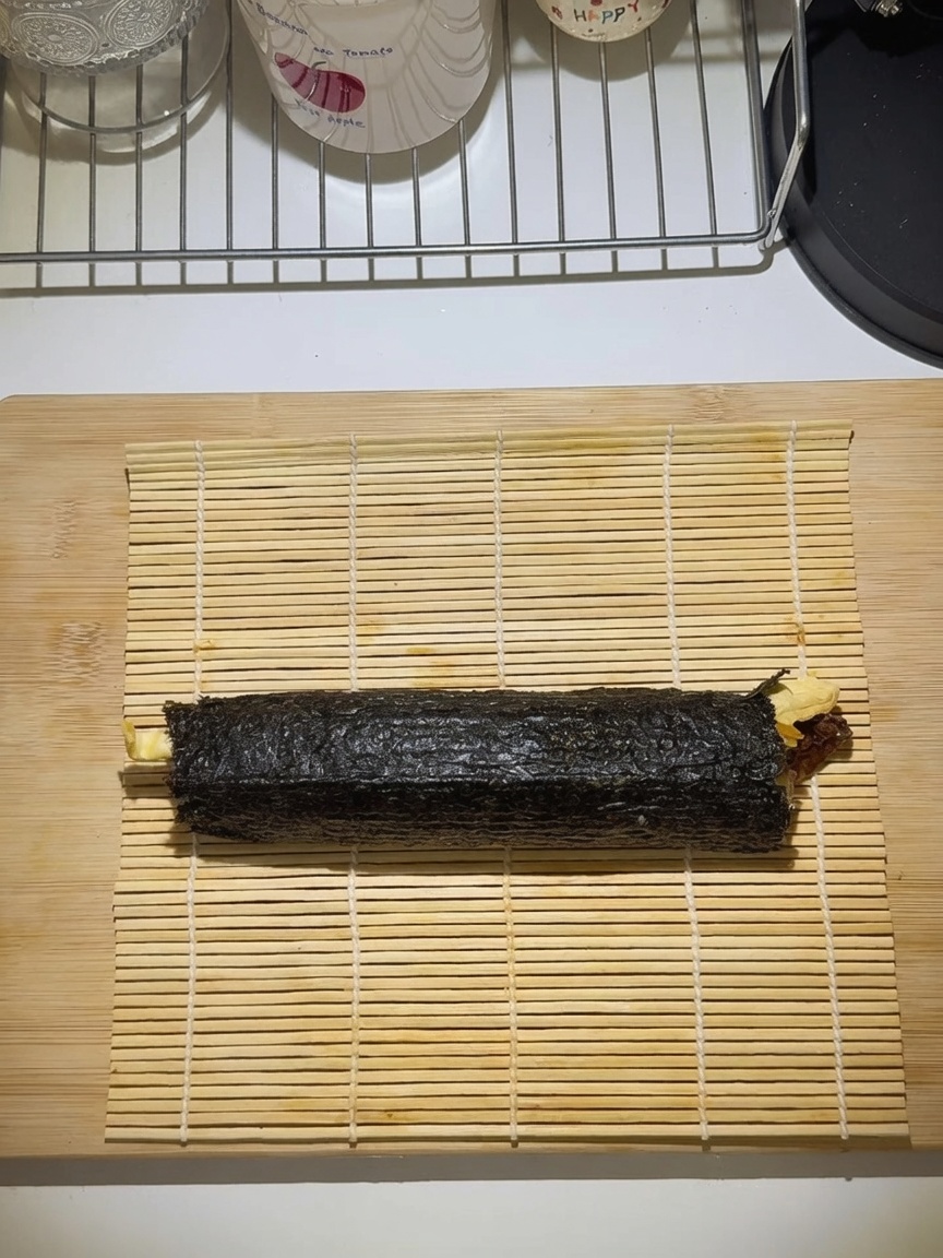 Un gimbap arrotolato strettamente su una stuoia di bambù.