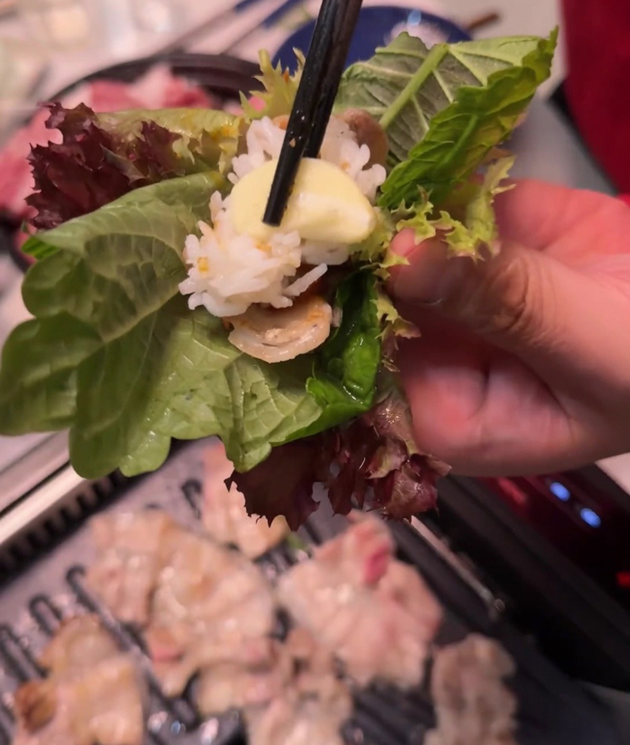 Una mano tiene un involtino di lattuga e perilla con carne, riso, salsa e aglio.