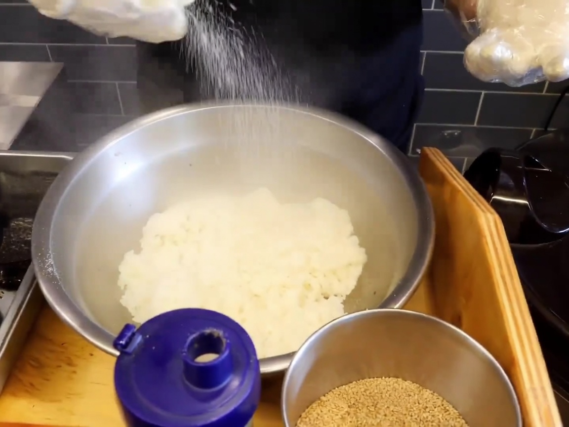 Primo piano di una ciotola in acciaio inox con riso caldo fumante, cosparso di sale e semi di sesamo.