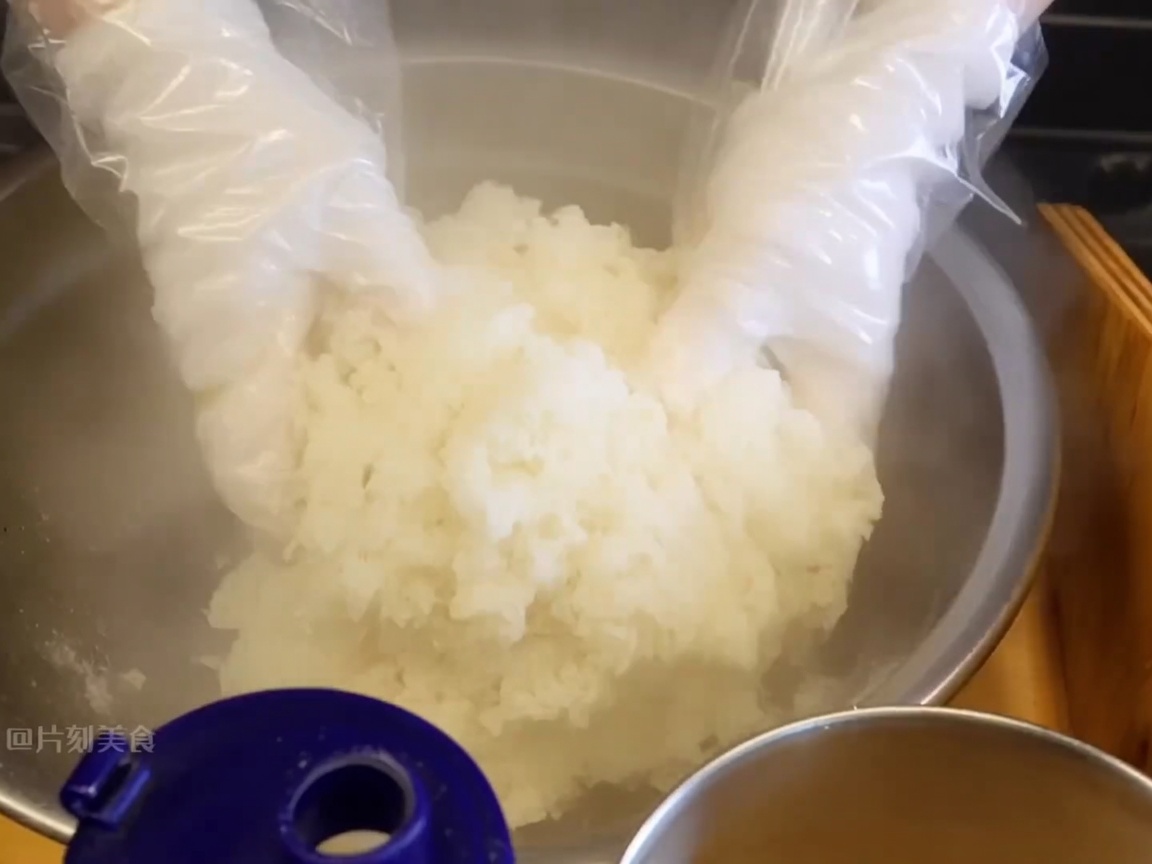 Mani guantate che mescolano il riso appiccicoso caldo per incorporare i condimenti.