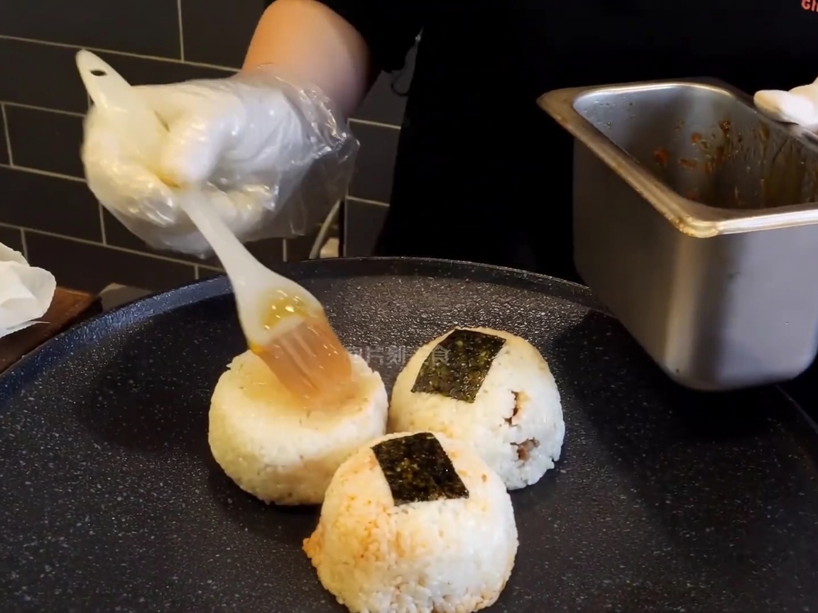 Polpette di riso su una piastra calda spennellate con una salsa bruna.