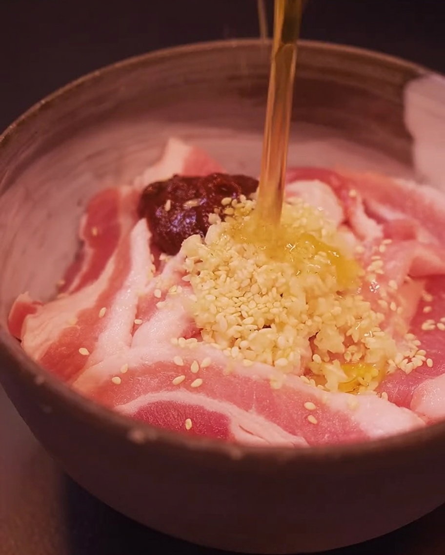 Fette di pancetta in una ciotola condite con gochujang, aglio tritato, semi di sesamo e olio di sesamo.