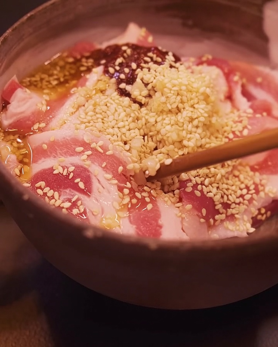 Primo piano di bacchette che mescolano le fette di pancetta marinate in una ciotola.
