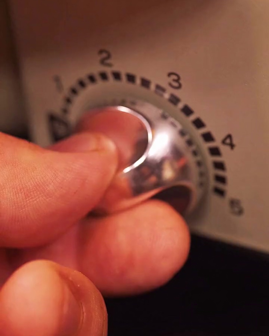 Una mano che regola la manopola della temperatura su una griglia elettrica.