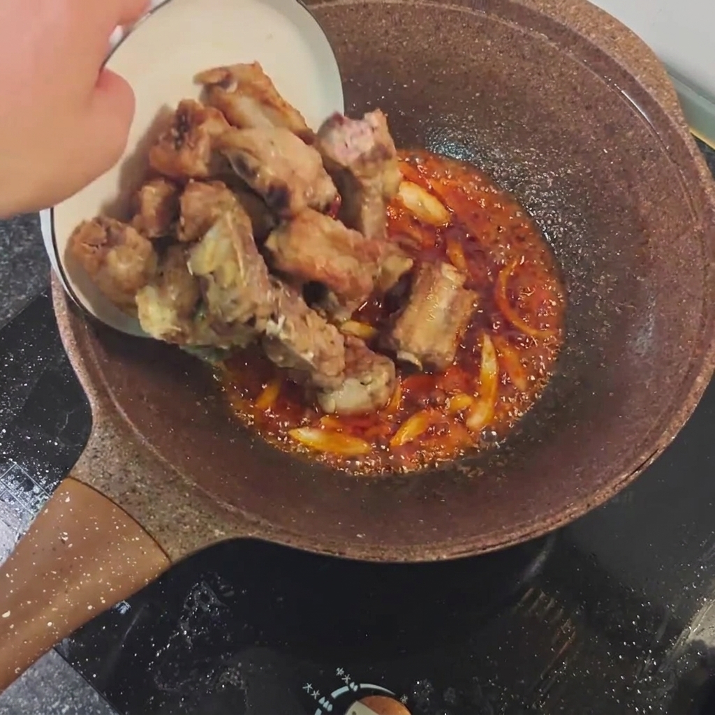 Costine fritte mescolate con salsa piccante e aromi in padella.