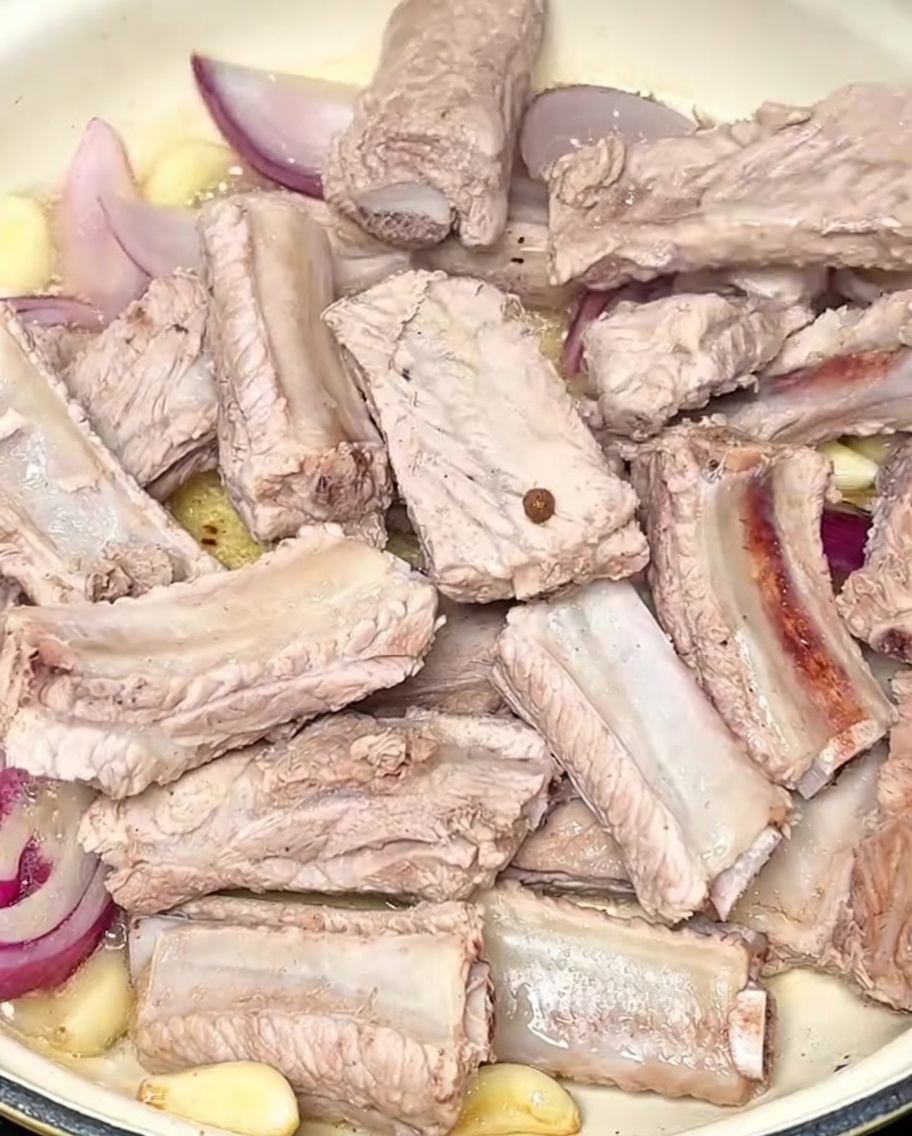 Costine di maiale rosolate in pentola con aglio e cipolla rossa.