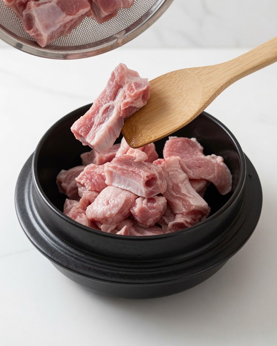 Costine di maiale saltate in una pentola con olio e zucchero bianco usando un cucchiaio di legno.