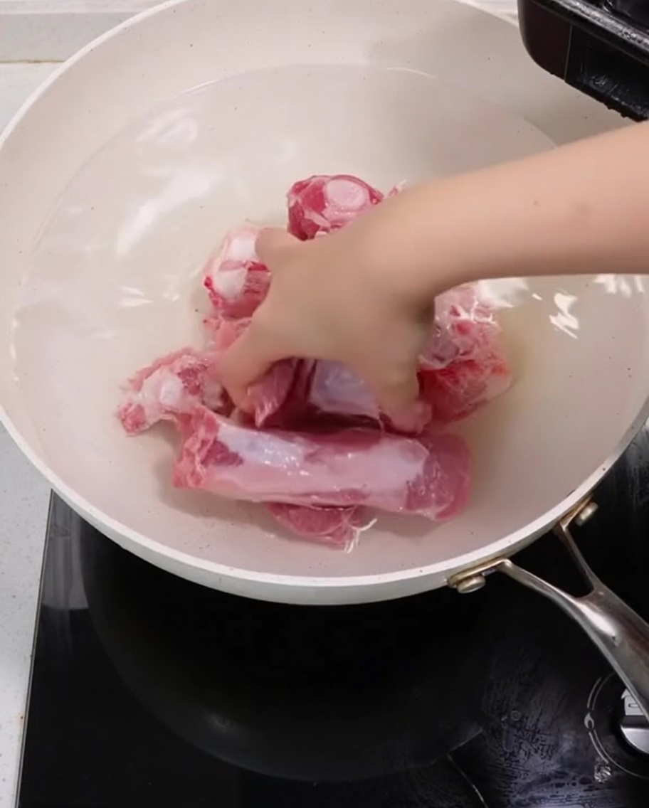 Costine di maiale che bollono in una pentola con cipollotti e zenzero per la sbollentatura.