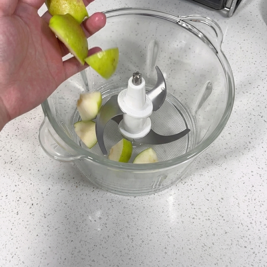 Un robot da cucina con pezzi di mela, pera, aglio e cipolla pronti per essere frullati.