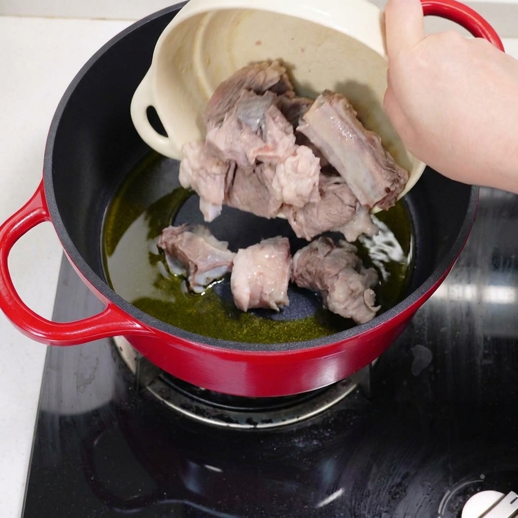 Costine di maiale sbollentate che vengono rosolate in una pentola con olio caldo.