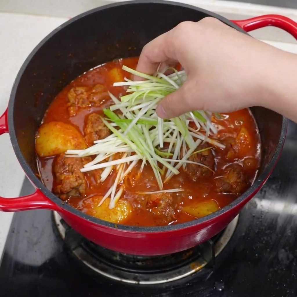 La pentola di costine brasate finita, guarnita con cipollotti, fette di peperoncino e una spolverata di pepe.