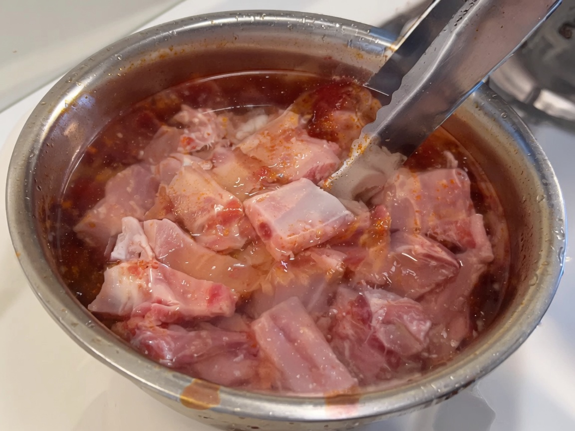 Costine di maiale fresche e crudesommerse in una ciotola di acqua pulita.
