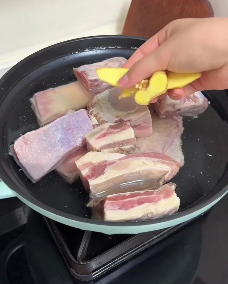 Costine di manzo in una pentola con acqua e fette di zenzero pronte per la scottatura.