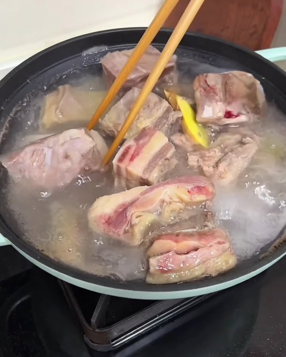 Mani che usano le bacchette per pulire le costine di manzo sbollentate sotto lacqua corrente.