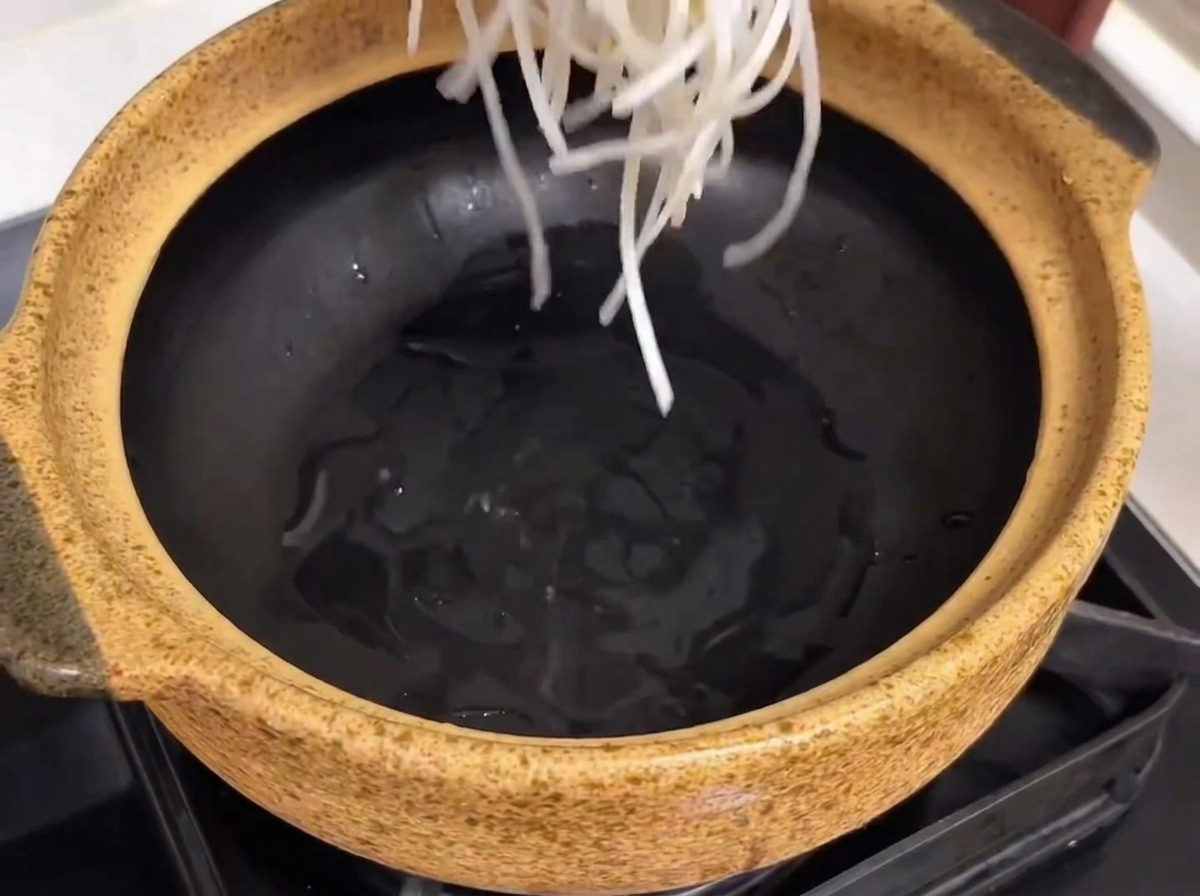 Una pentola di ceramica preparata con vermicelli di soia, costine di manzo tenere e pezzi di ravanello posizionati allinterno.