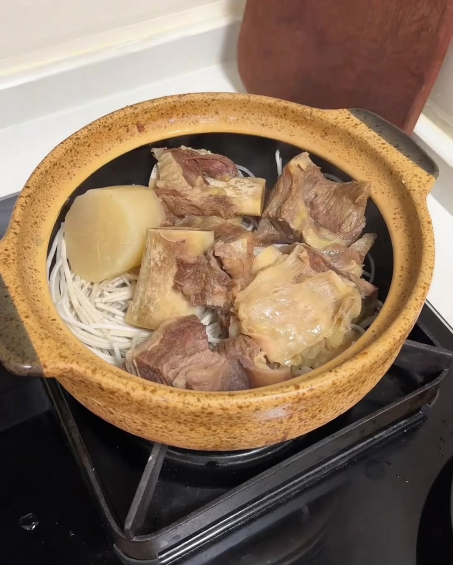 Un brodo di ossa di bue chiaro e ricco versato da un cuociriso in una pentola di ceramica riempita con costine di manzo, ravanello e noodles.
