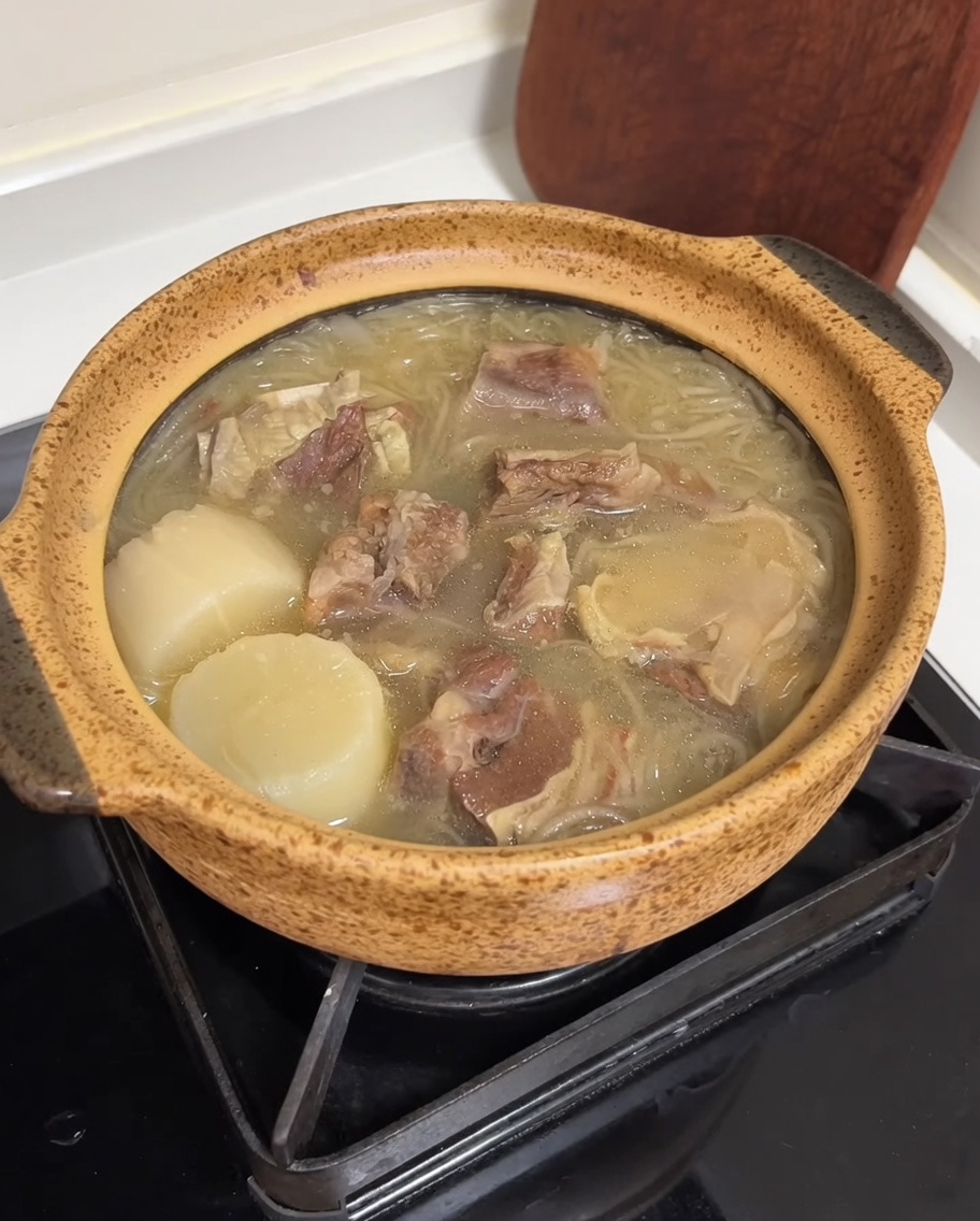 Una pentola di ceramica riempita di zuppa di manzo, guarnita con strisce di uovo giallo brillante e vivaci cipollotti verdi affettati.