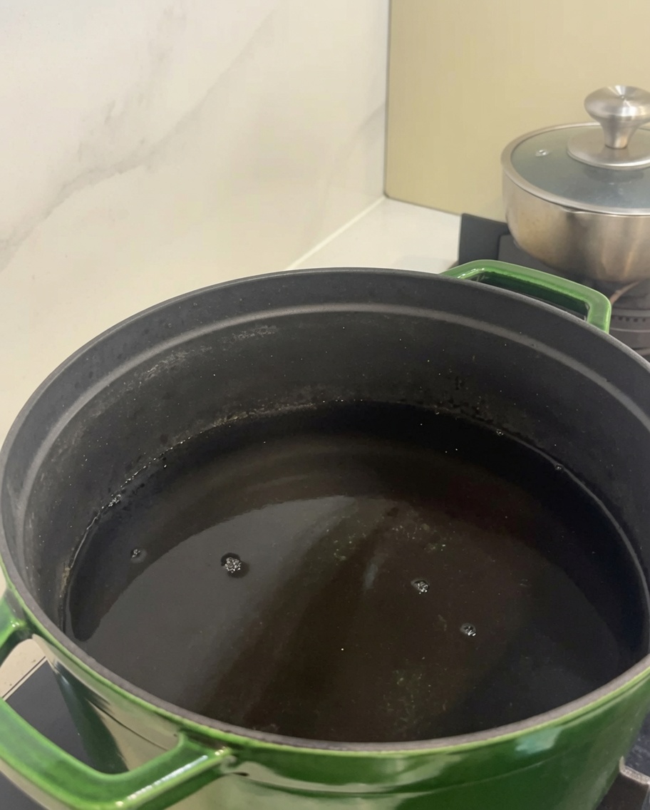 Pezzi di costine di manzo crude allinterno di una grande pentola verde riempita dacqua fredda.