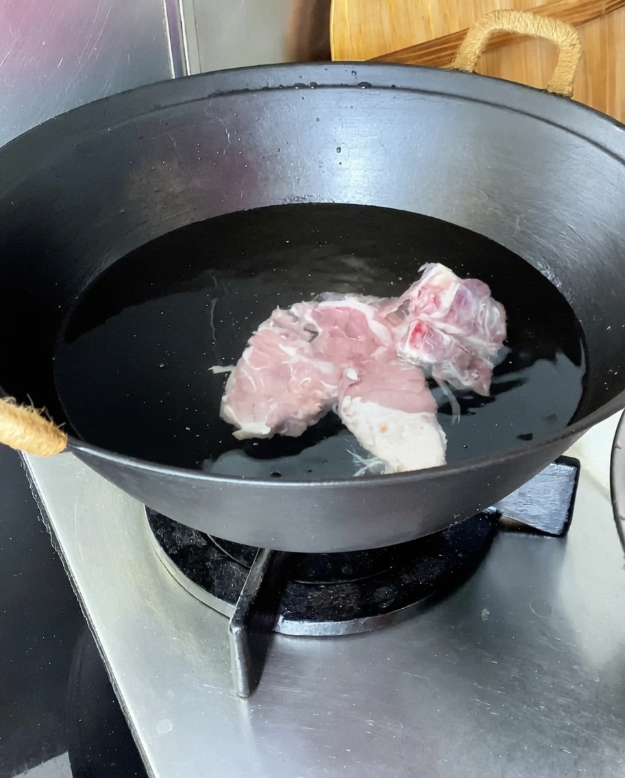 Costine di maiale in un wok con acqua fredda, zenzero, cipollotti e vino da cucina.